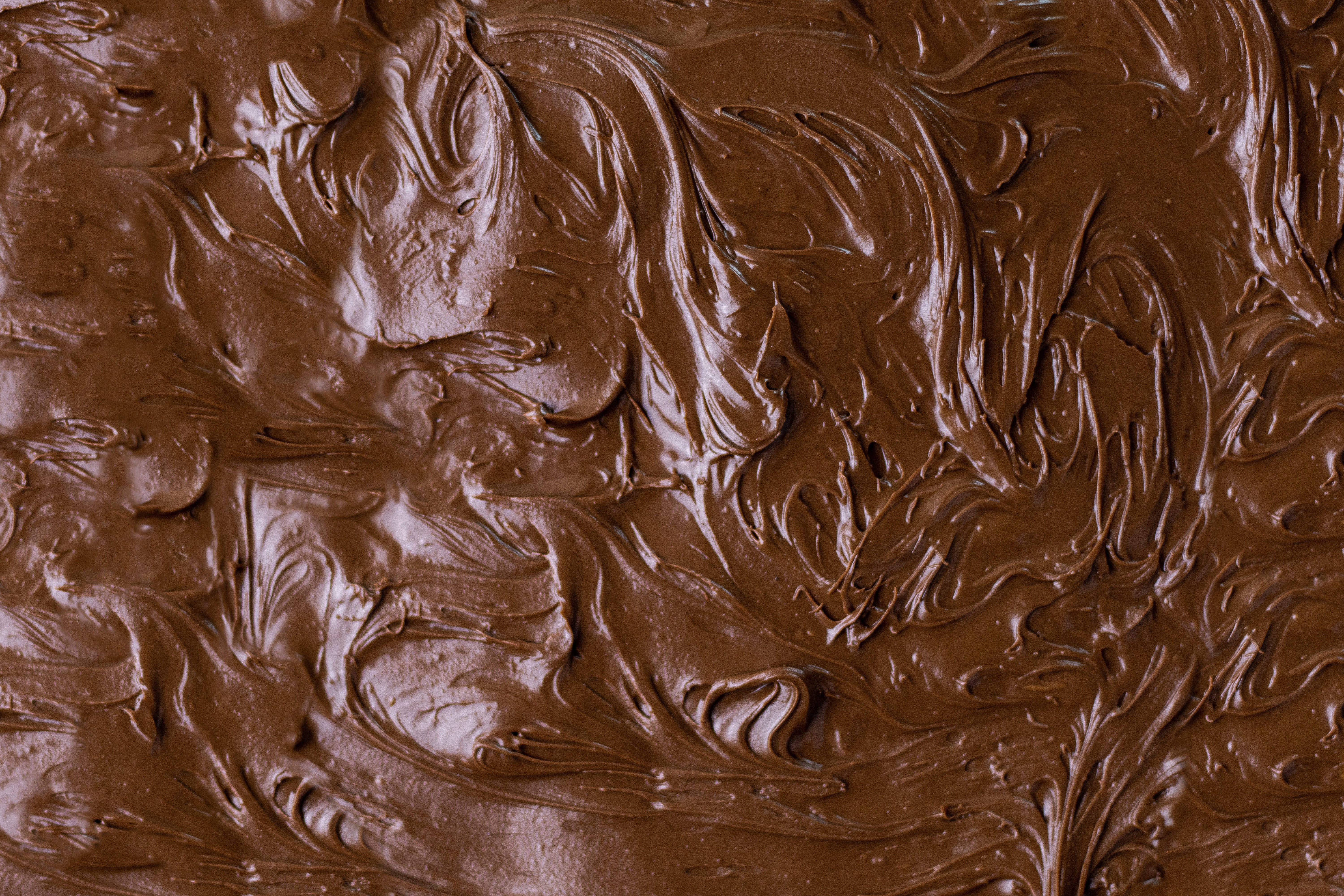 Close-up of rich brown chocolate frosting with smooth, swirling texture, creating a luscious and inviting appearance.